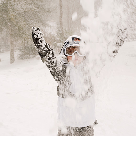 Boy in snowy forest throws snow into air with arms up.