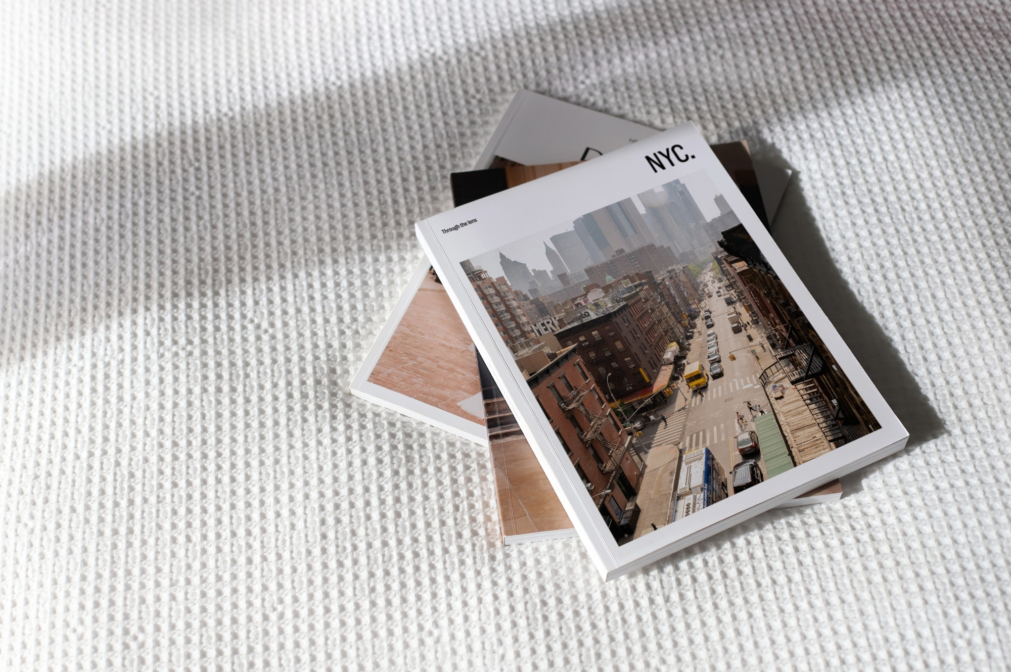 Stack of travel magazines on white bedsheet under sunlight.