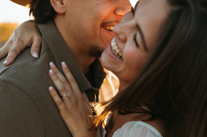 A couple embracing and smiling showing off an engagement ring.