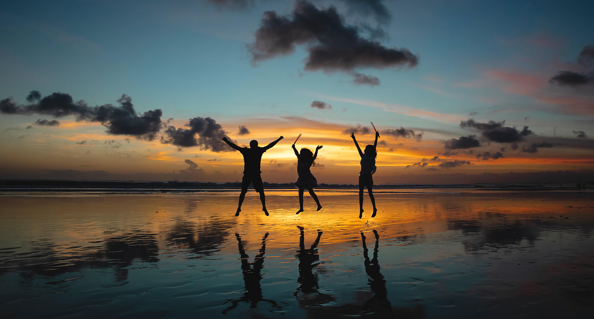 Silueta de tres personas saltando en el aire en la playa durante la puesta de sol.